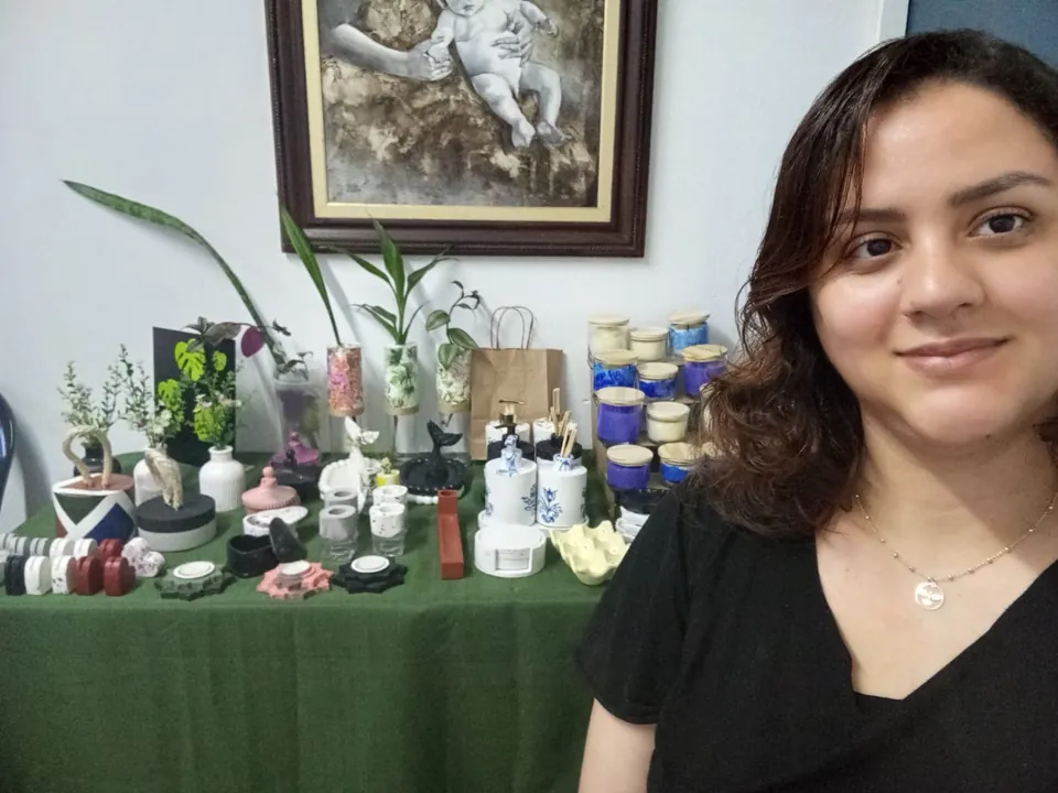 Dayana Calil, artesã da Morada Ateliê, sorrindo ao lado da mesa com as suas peças