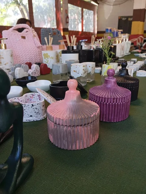 Potes canelados rosa e lilás com tampa sobre mesa de feira