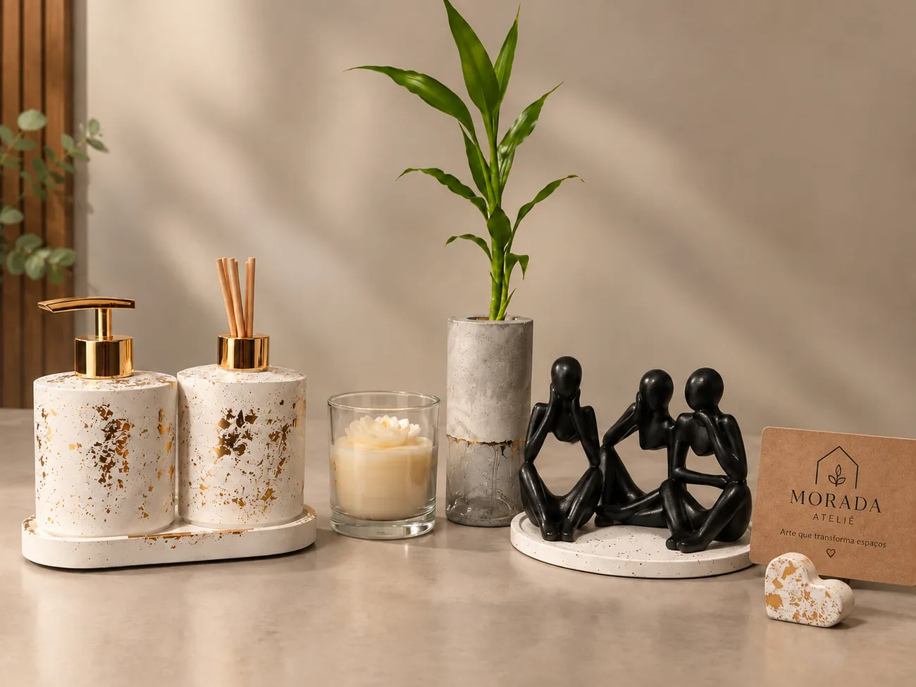 Kit de lavabo branco com manchas douradas, vela, vaso de concreto com bambu e esculturas pretas sobre bandeja